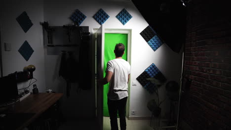 Caucasian-creative-freelancer-working-in-his-professional-home-studio,-walking-barefoot-opening-a-white-door-with-green-screen