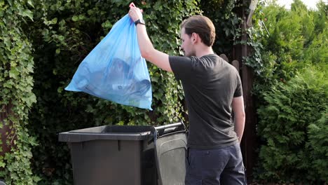 Caucasian-male-taking-out-trash-in-plastic-bag-to-bin-in-garden