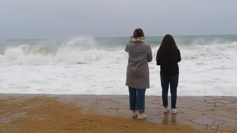 Two-people-from-the-back-watching-the-big-waves-break-on-the-Costa-Brava