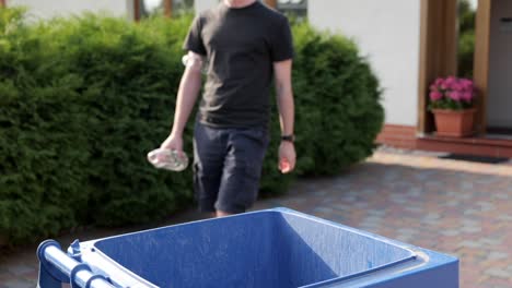 Unrecognizable-man-walks-out-to-throw-plastic-bottles-into-trash-bin-in-garden