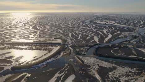Aerial-approaching-shot-of-bridge-over-large-river-braids-and-river-delta-during-sunset-time-in-iceland---Tilt-Down-shot