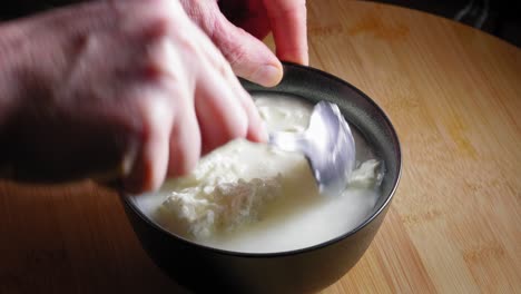 A-close-up-shot-of-a-black-mixing-bowl-filled-with-white-low-fat-cheese,-as-a-chef-carefully-breaks-up-the-clumps-with-the-back-of-a-spoon-and-stirs-to-create-an-even-texture