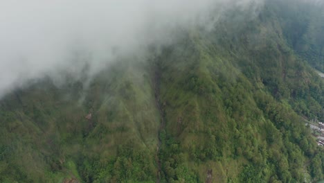 Misty-environment-with-lush-green-mountainside-at-caldera-lake-Batur,-aerial