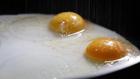 Extreme-Close-Up-Of-Sunny-Side-Up-Eggs-Cooking-In-A-Pan,-Sprinkled-With-Salt-And-Pepper