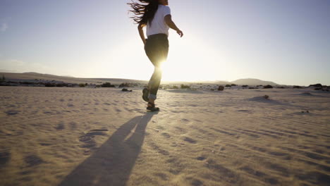 Young-black-woman-running-with-sandals-in-sand-dunes-desert-the-sunset-by-scenic-wavy-texture-sand-surface