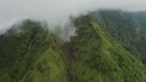 Green-caldera-mountain-walls-formed-by-erosion-with-clouds-above,-aerial