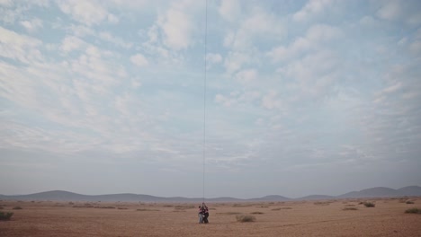 Gruppe-Von-Menschen,-Die-Einen-Heißluftballon-Mit-Einem-Seil-In-Der-Marokkanischen-Wüste-Herunterziehen