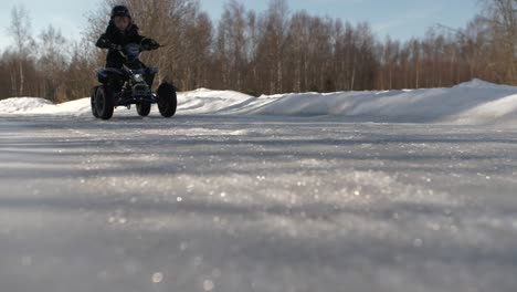 Young-Caucasian-boy-rides-ATV-on-icy-road,-low-tracking-shot