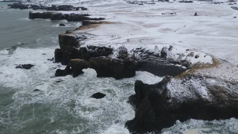 Aerial-view-of-strong-waves-crashing-against-steep-coastline-of-Arnarstapi,-Iceland-in-Winter-Season