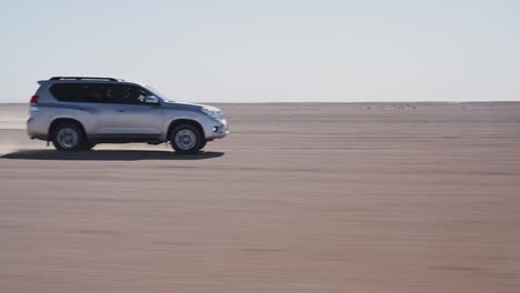 4x4-vehicles-racing-on-sandy-surface-of-Sahara-desert,-handheld-side-view