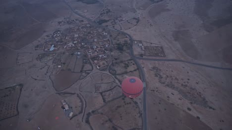 Hot-air-balloon-fly-above-small-town-in-Morocco,-handheld-view-from-above