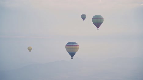 Group-of-hot-air-balloon-fly-over-foggy-landscape-of-Marocco,-handheld-view