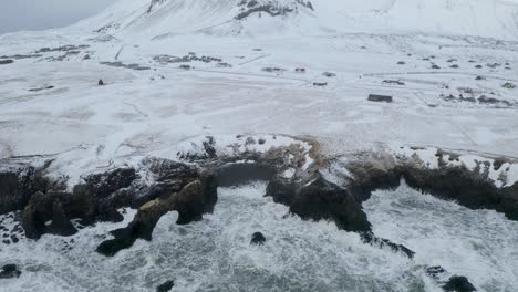 Luftaufnahme-Des-Schneebedeckten-Vulkans-Snæfellsjökull-Und-Wellen-Des-Ozeans-Mit-Steilen-Dunklen-Klippen-Im-Vordergrund---Besuch-Von-Island-Im-Winter