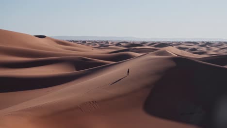 Lonely-nomad-walking-on-sandy-dunes-of-endless-Sahara-desert,-handheld-view
