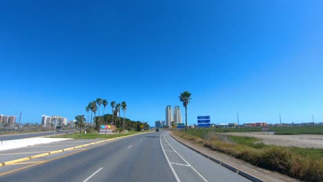 POV-Driving-toward-condo-towers-on-South-Padre-Island-and-past-marshy-area-along-Laguna-Madre-on-bright-and-sunny-day-in-southern-Texas