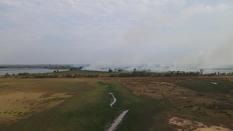 Aerial-footage-sliding-to-the-right-over-a-dry-land-in-summer-while-farms-in-the-distance-burning-in-Pak-Pli,-Nakhon-Nayok,-Thailand