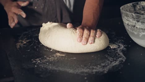 Hand-of-chef-preparing-fresh-dough-for-pastry-cooking-on-black-table,-close-up-view