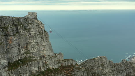Climbing-Cable-Car-Towards-The-Table-Mountain-Cable-Station-With-Camps-Bay-Beach-Backdrop-In-Cape-Town,-South-Africa