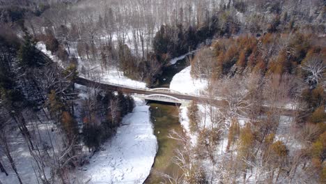Scenic-Bridge-with-winding-road-Spanning-wide-river-set-in-a-Winter-Landscape-with-snow-and-Evergreen-Trees