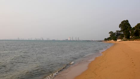 Beautiful-Calm-Waves-Along-the-Beach-of-Bangsaray-in-Pattaya,-Thailand-with-City-Buildings-on-the-Horizon-in-the-Background