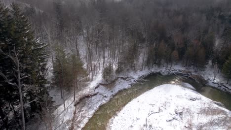 Snow-Covered-Winter-Landscape-River-Reveal-to-Forest-Aerial-Drone-Shot