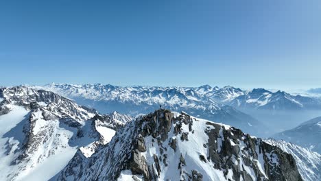 Drone-shot-of-a-mountaineer-standing-on-a-rocky-peak-in-the-Alps
