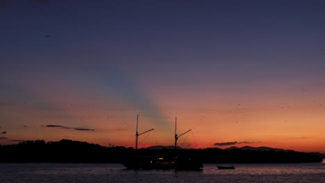 Silhouette-Von-Hügeln-Und-Booten-Bei-Sonnenuntergang-Mit-Vielen-Flughunden-Oder-Fledermäusen-Auf-Der-Insel-Kalong,-Labuan-Bajo,-Indonesien