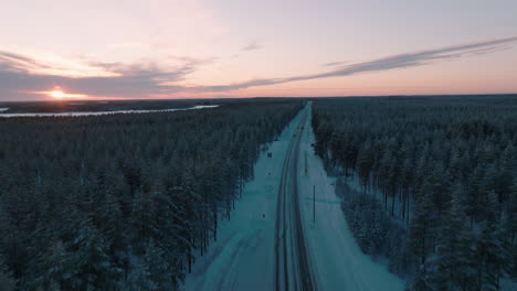 Volando-Sobre-La-Carretera-De-Nieve-En-Un-Bosque-Denso-Durante-La-Puesta-De-Sol-En-Finlandia