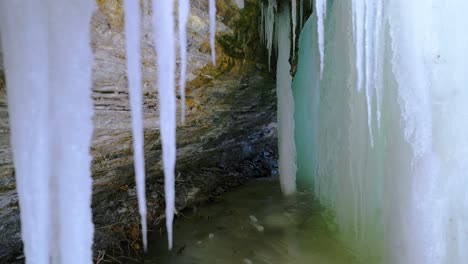 Hinter-Einem-Gefrorenen-Wasserfall-Mit-Großen-Eiszapfen-Und-Einer-Eishöhle-Mit-Felsiger-Klippe