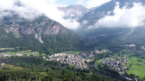 Bormio-at-Valtellina,-Sondrio,-Lombardy,-Italy---Aerial-Drone-View-of-the-Ski-Village,-Green-Valley-and-Cloudy-Mountains