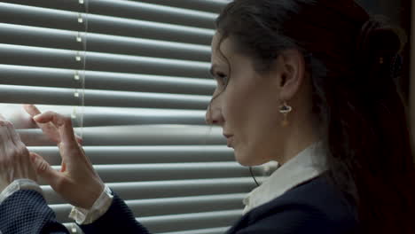 Strict-business-woman-looking-through-window-blinders-and-turning-her-head-annoyed-at-someone-offscreen