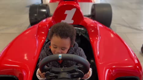 Two-year-old-exotic-afroeuropean-baby-enjoying-in-a-F-1-toy-red-car-inside-a-Mall