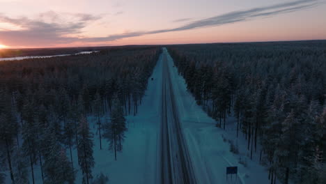 Antenne-Der-Winterstraße-Zwischen-Dichtem-Dickicht-Während-Des-Sonnenuntergangs-In-Finnland