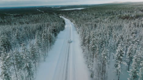 Vista-Aérea-De-La-Autocaravana-Conduciendo-Por-Un-Camino-Nevado-En-Laponia,-Finlandia