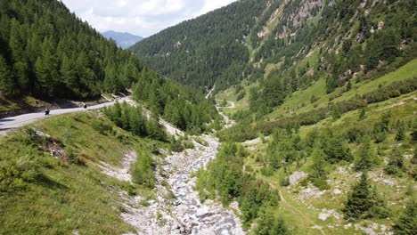 Schweizer-Nationalpark---Luftdrohnenansicht-Von-Motorrädern,-Die-Entlang-Des-Grünen-Bergtals-Und-Des-Flusses-Fahren