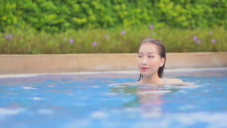 A-young-attractive-woman,-neck-high-in-a-swimming-pool-water,-turns-her-head-to-look-into-the-camera