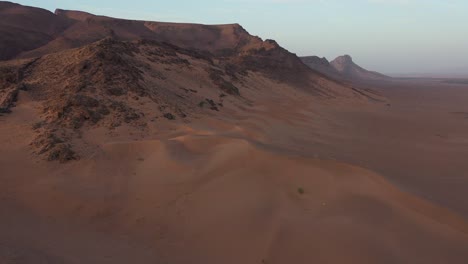 Drohne-Fliegt-über-Wüstendünen-Mit-Felsigen-Bergen-Im-Hintergrund,-Zagora-In-Marokko