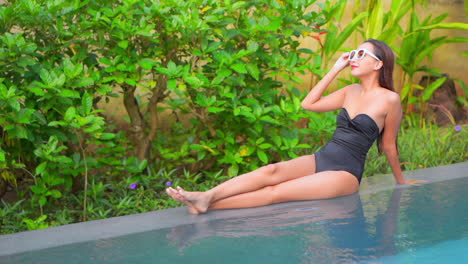 A-full-body-profile-of-a-fit,-attractive-woman-sitting-on-the-edge-of-a-swimming-pool