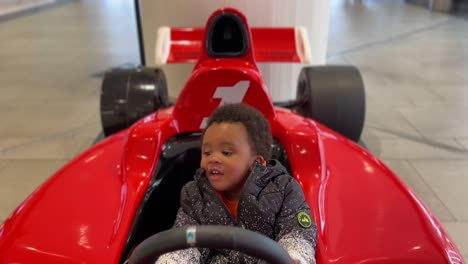 Exotic-two-year-old-afroeuropean-baby-happy-playing-in-a-toy-F-1-red-car