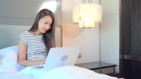 While-sitting-up-in-bed,-a-young-woman-works-on-her-laptop