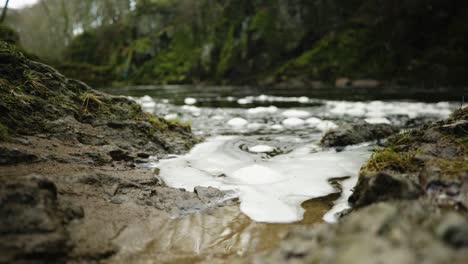 A-time-lapse-of-foam-bubbles-floating-on-the-surface-of-the-North-Esk-river-while-slowly-lapping-against-the-river-bank