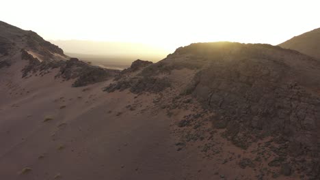 Sunlight-illuminating-valley-behind-rocky-desert-mountains,-Zagora-in-Morocco