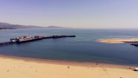 A-drone-flight-over-a-beach-adjacent-to-a-pier,-Santa-Barbara-California
