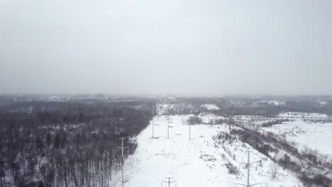 Electric-Power-Lines-Hydro-Corridor-in-Gloomy-Winter-forest-snowy-Landscape-aerial-fly-over