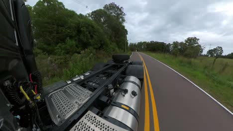 Rear-view-perspective-of-truck-driving-a-on-a-country-road-under-a-cloudy-sky-with-woods-on-both-sides