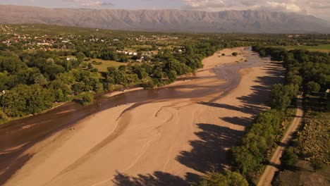 People-relaxing-on-sandy-river-bed-with-beautiful-landscape-in-background,-Cordoba-in-Argentina