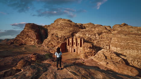 Cinemagraph-seamless-video-loop-of-a-young-female-woman-in-Petra-Jordan,-looking-at-the-historic-UNESCO-heritage-site-Ad-Deir-Monastery-carved-into-sandstone-with-moving-hair-on-a-scenic-sunny-evening