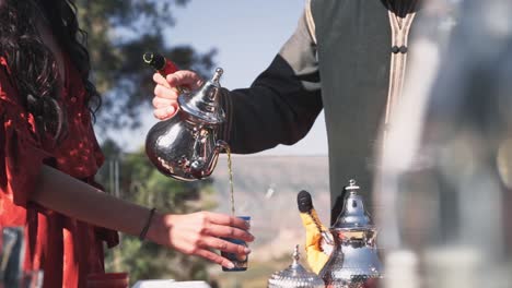 Man-pouring-fresh-Moroccan-mint-tea-for-beautiful-woman,-handheld-view