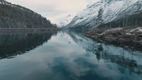 Mountain-range-reflects-in-lake-water-in-Norway,-Loen,-aerial-FPV-view