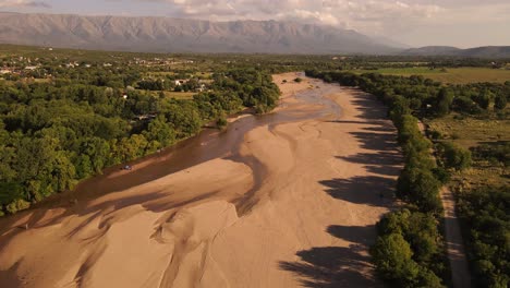 Aerial-view-of-dried-out-River-surrounded-by-green-forest-trees-and-mountain-range-in-background---Heat-climate-in-Argentina